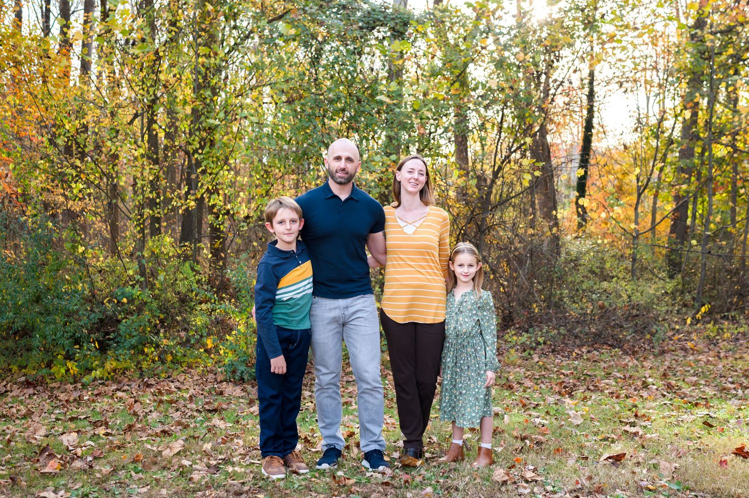 Family group walks together through autumn woods with golden sunlight filtering through colorful fall foliage.
