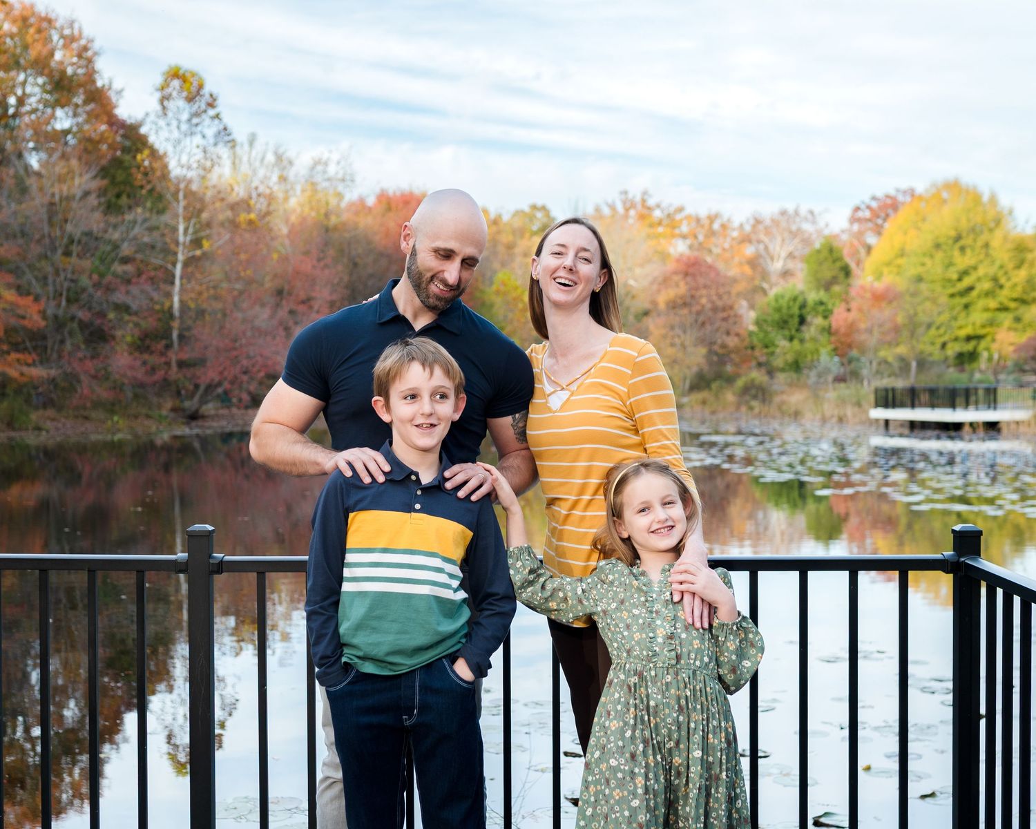 A family poses together on a deck overlooking a lake surrounded by vibrant fall foliage.