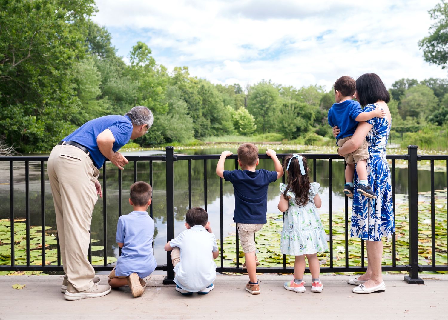 People are leaning over a railing together to look at something below at a scenic outdoor location.