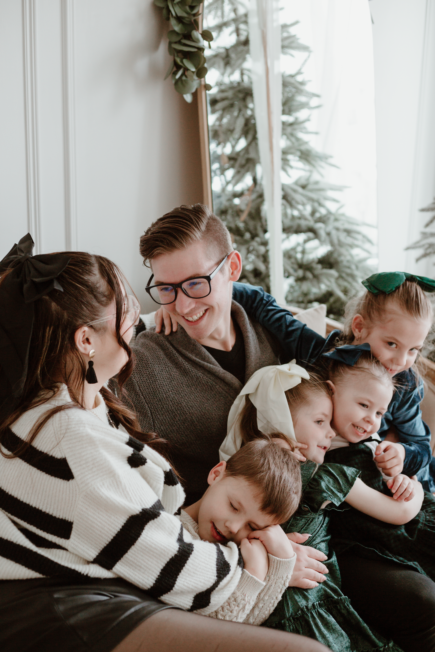 Family of five cozied up on the couch by the christmas tree laughing and hugging while mom and dad look at each other.