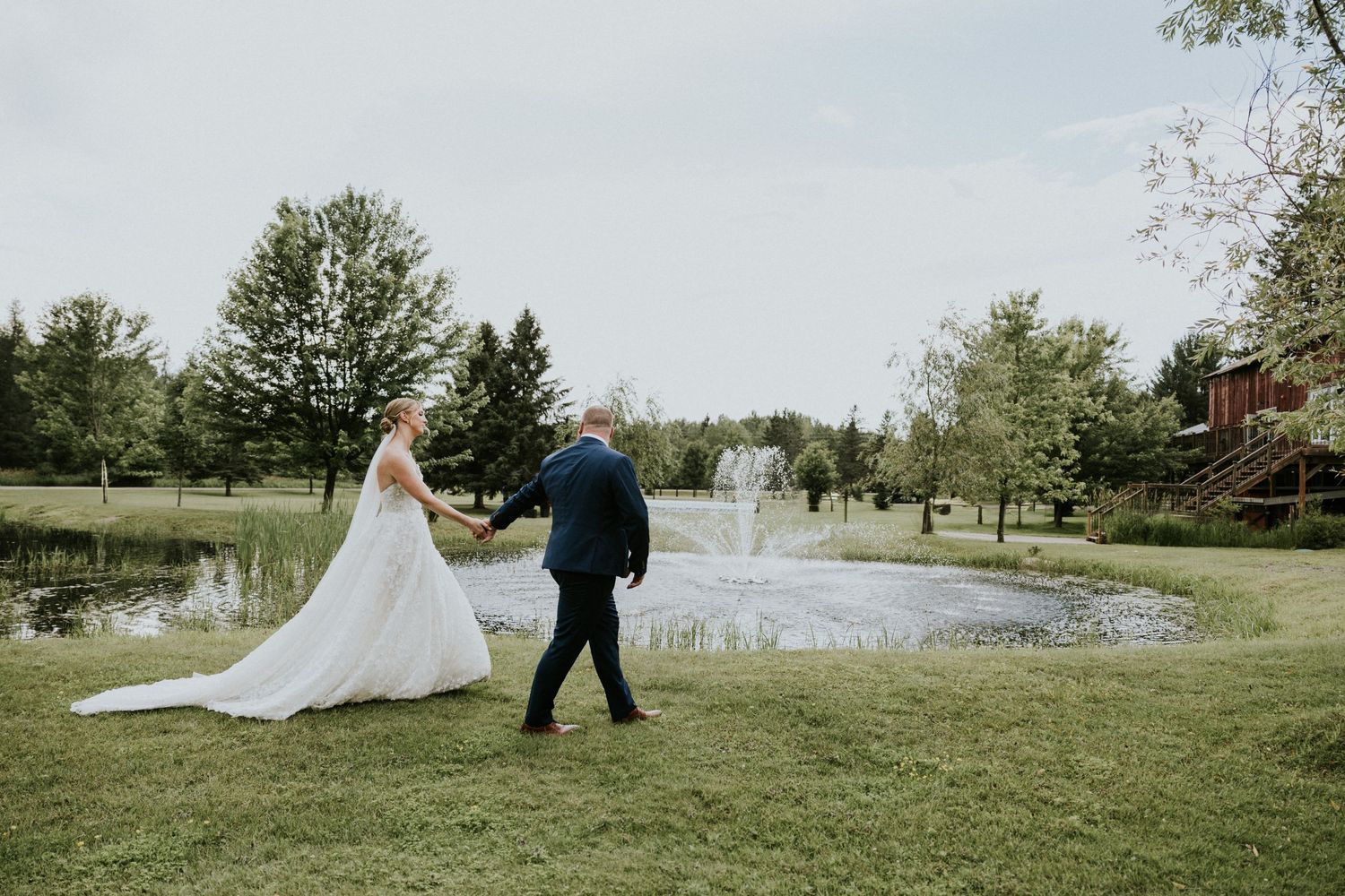 Couple walks hand in hand on grassy lawn near peaceful pond.