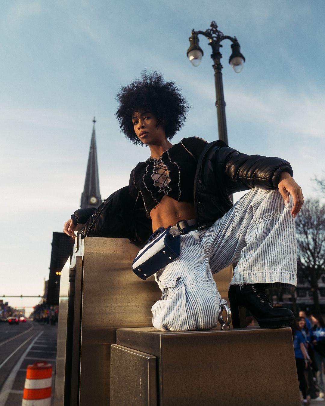 Urban fashion shot featuring natural hair and streetwear style posed on architectural elements.