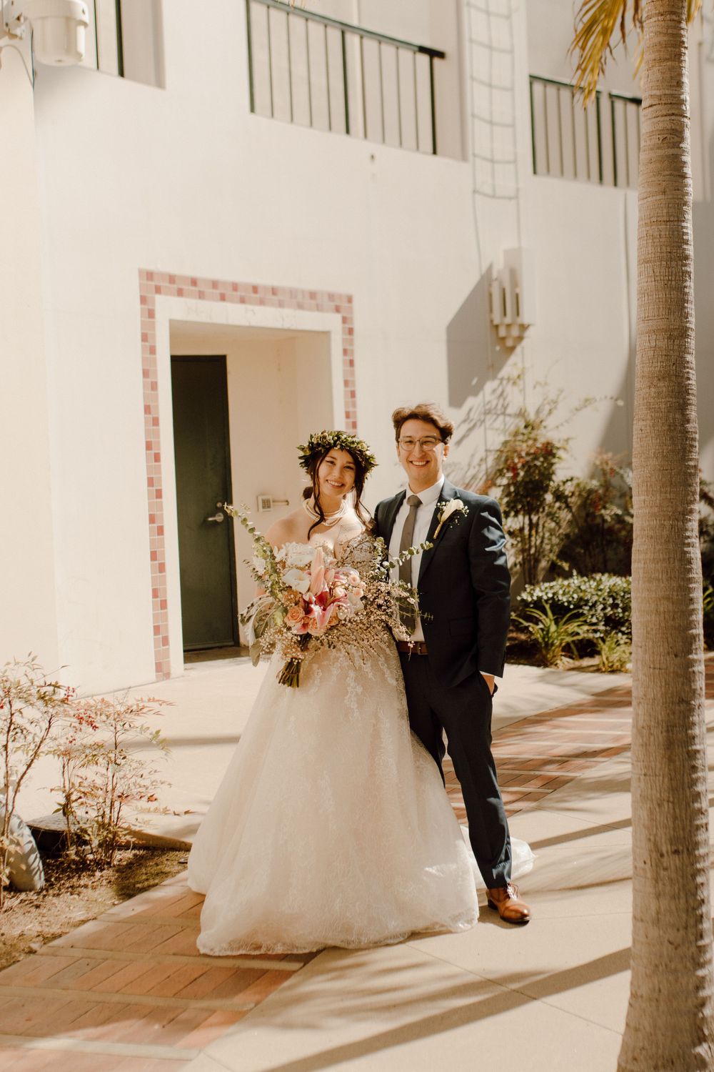 A wedding couple poses on a sun-drenched terrace with Mediterranean architectural details.