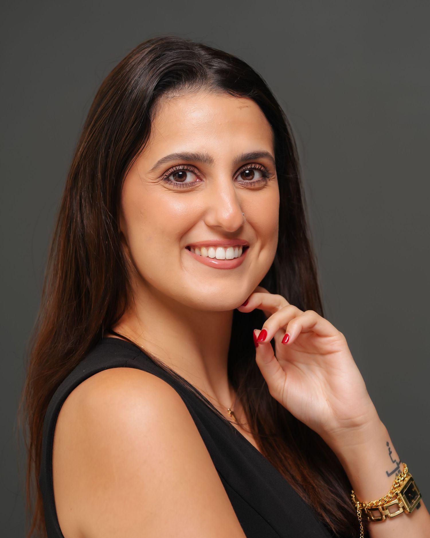 Professional headshot of a smiling woman with long dark hair wearing a black top and gold bracelet.
