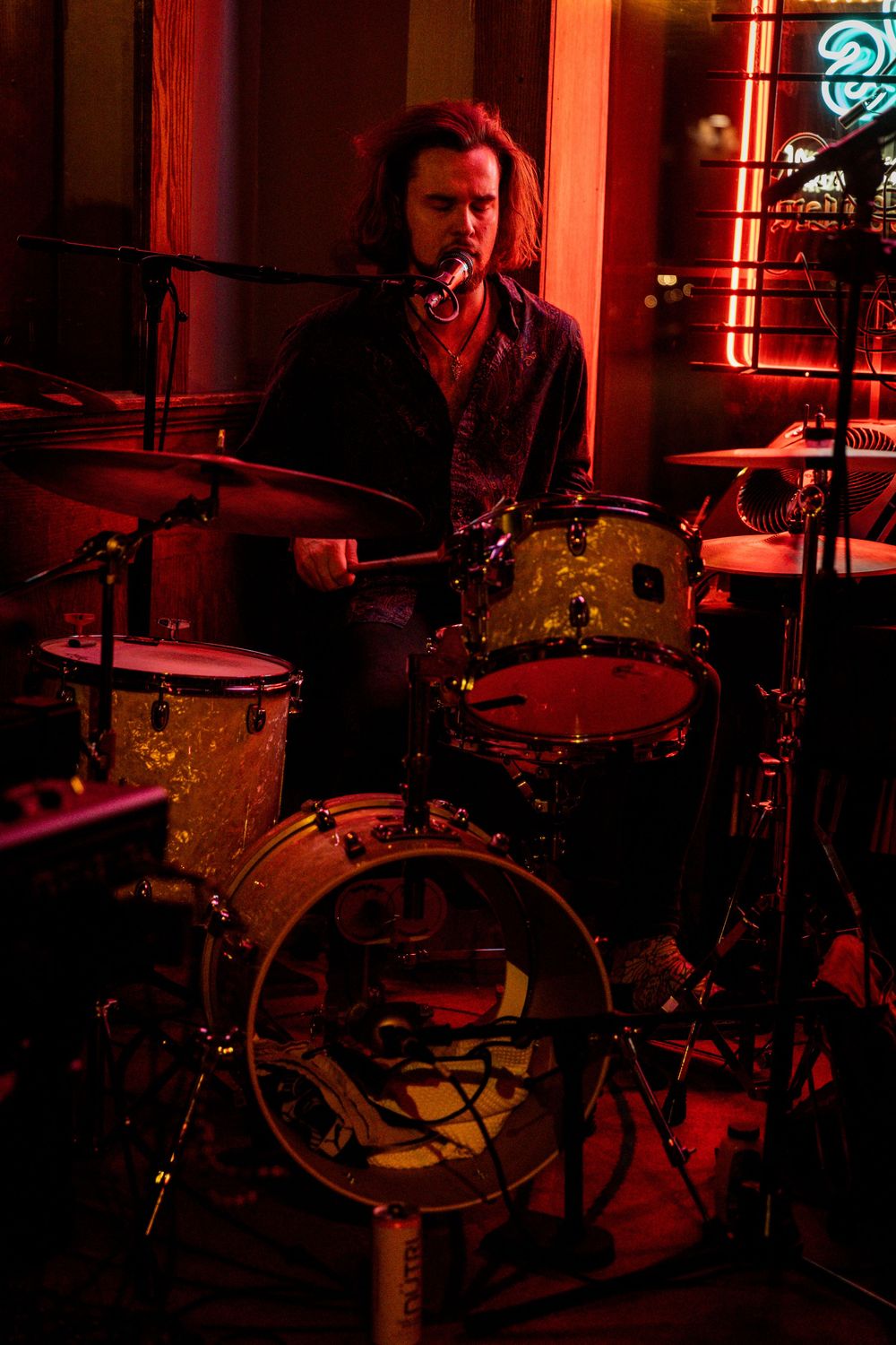 Drummer performing on stage bathed in dramatic red lighting.