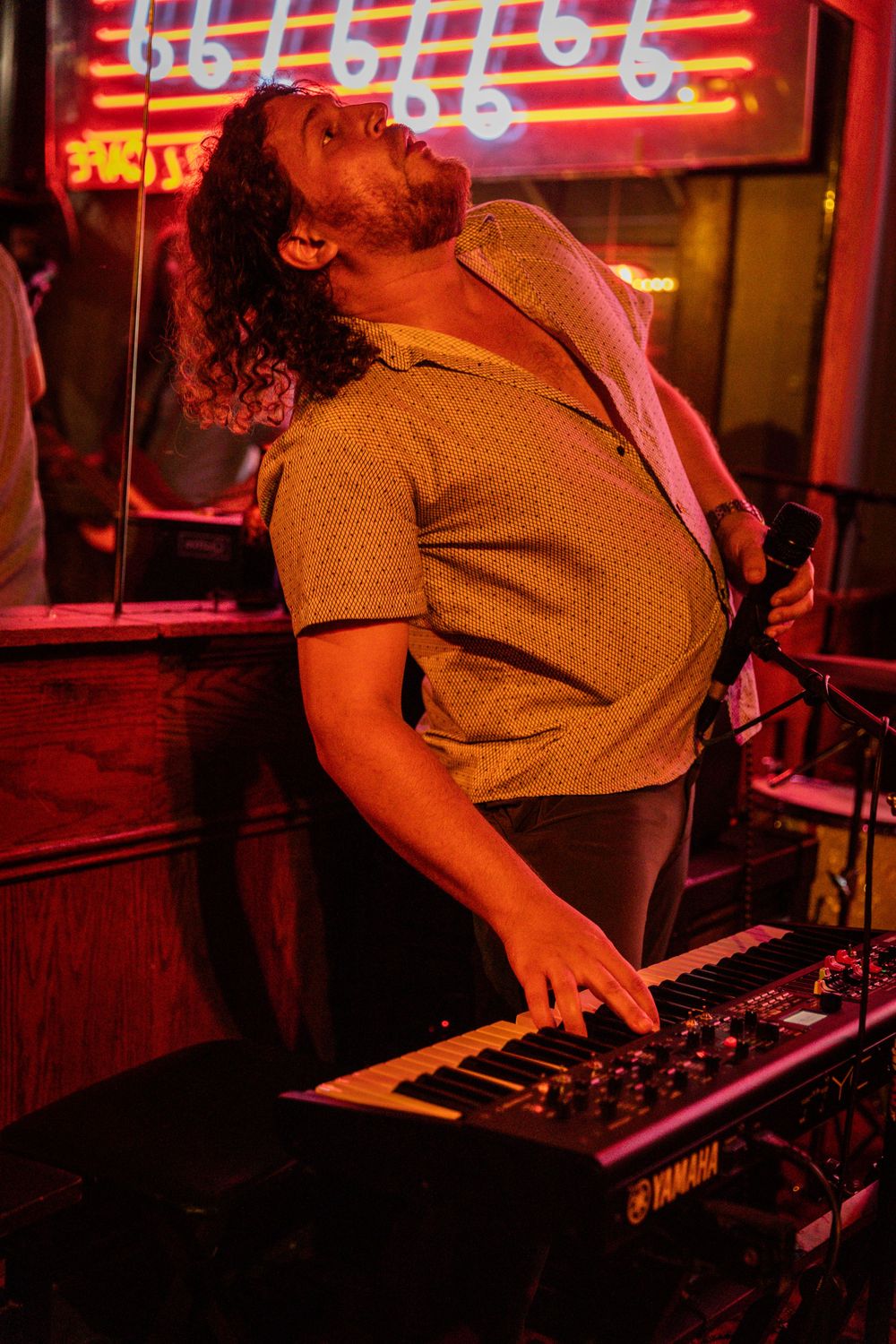 Musician playing keyboard under glowing red neon signage.