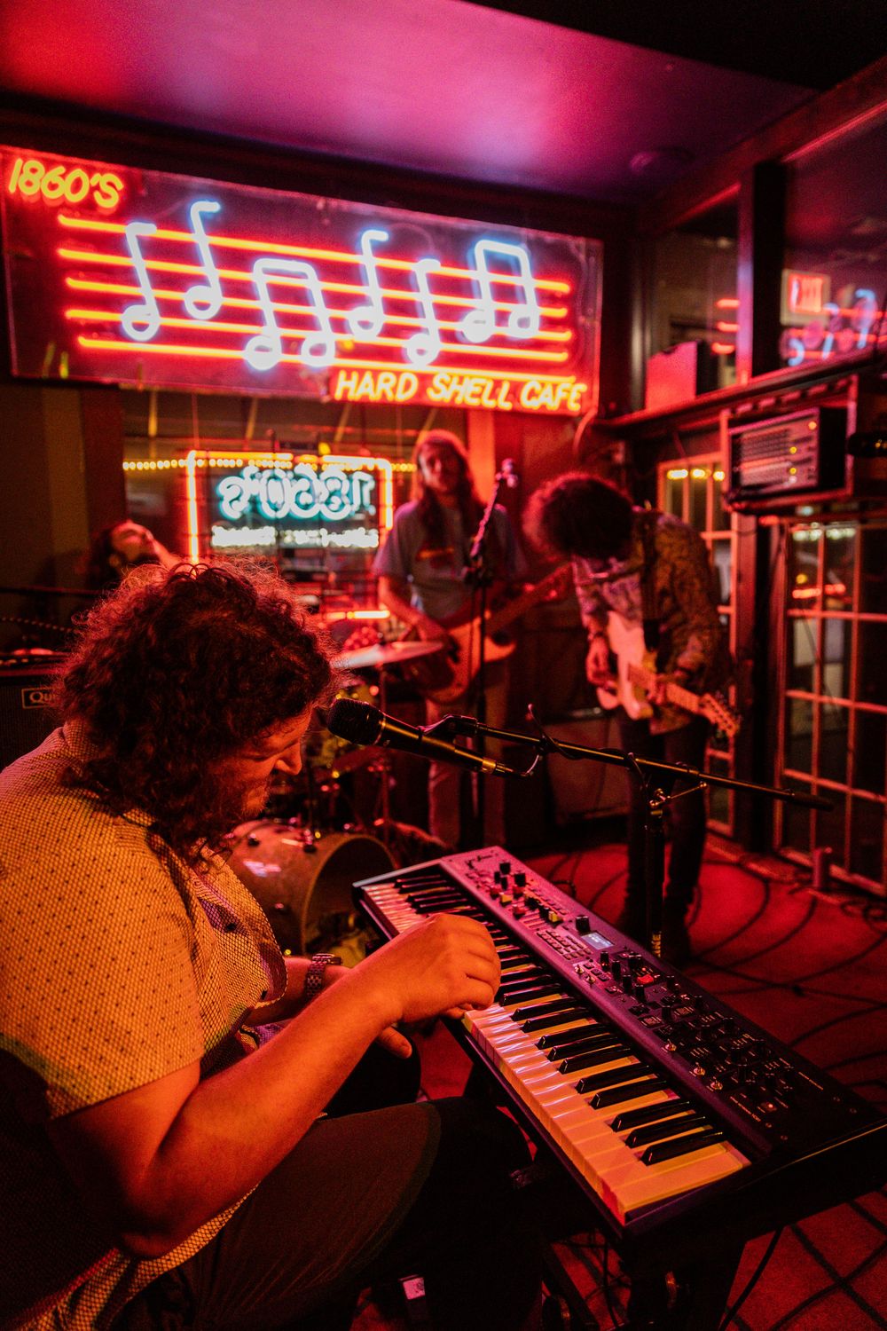 Live music performance at venue with vintage neon signs and red lighting effects.