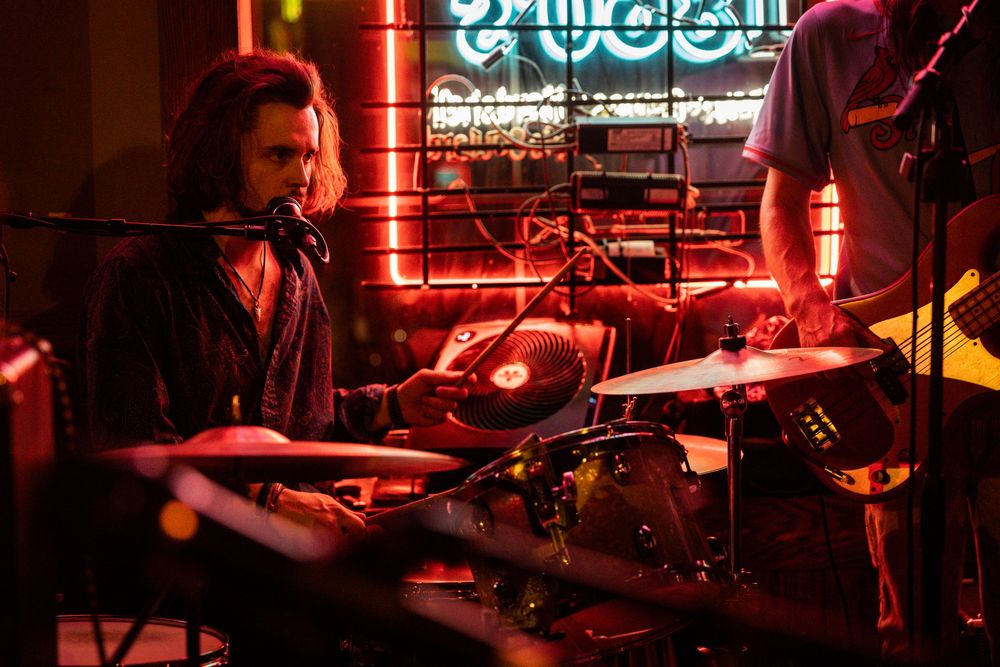 Drummer performs on stage with red neon lighting and cymbals.