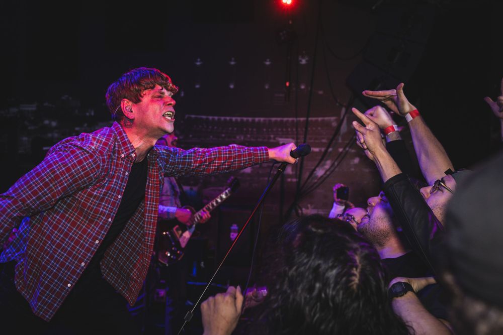 Concert performers engage with crowd during high-energy show under dramatic red stage lighting.