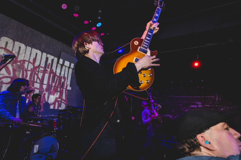 Band members perform passionately on stage with vibrant lighting and musical equipment visible.