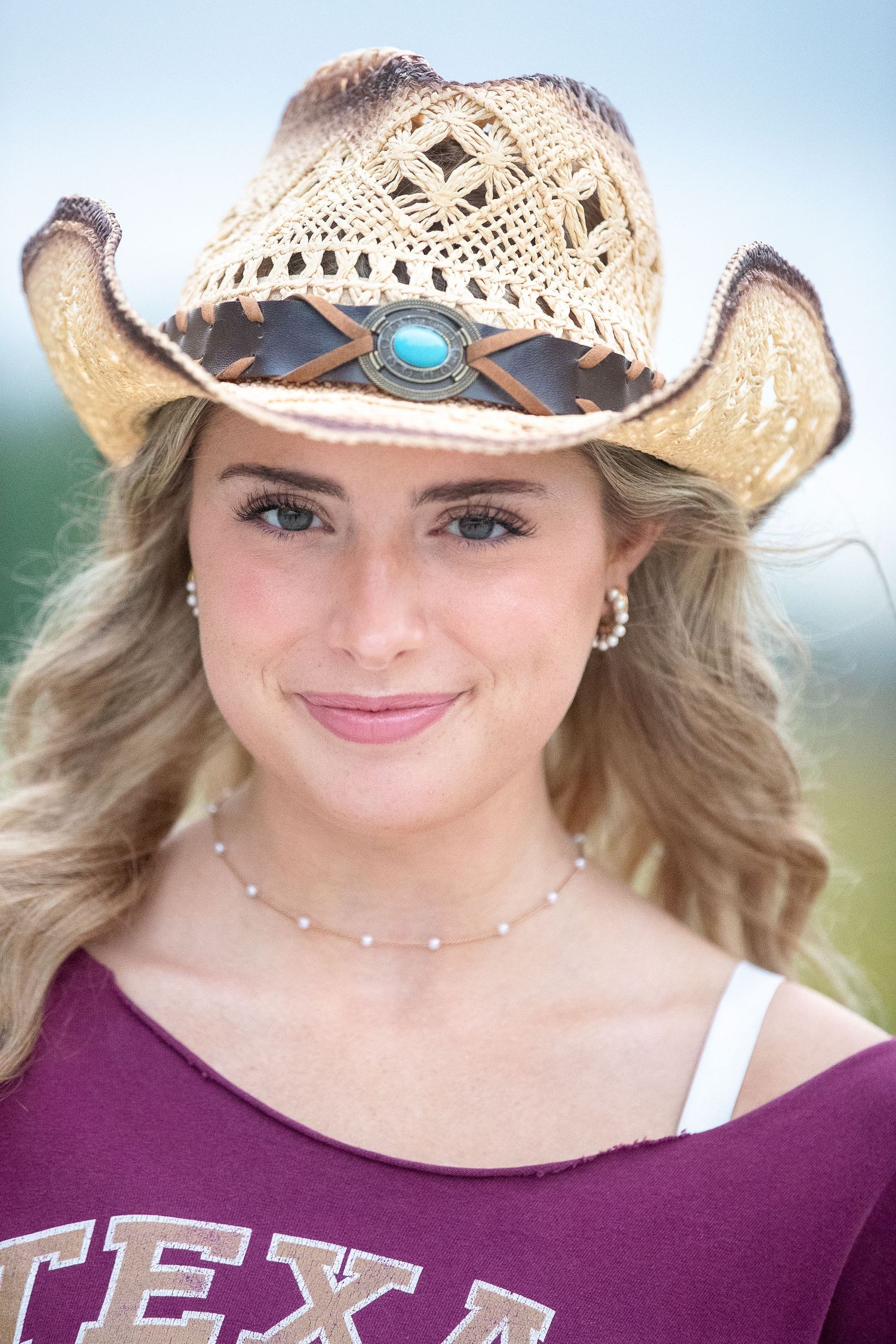 Smiling person wearing a maroon Texas shirt and straw cowboy hat with turquoise accent in outdoor setting.