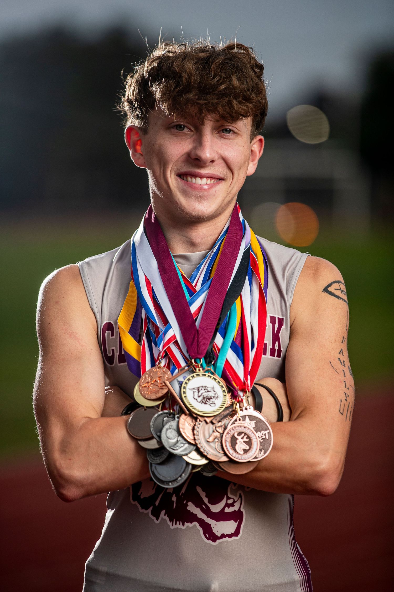 Athletic person displaying multiple sports medals and ribbons earned in competition against dark background.