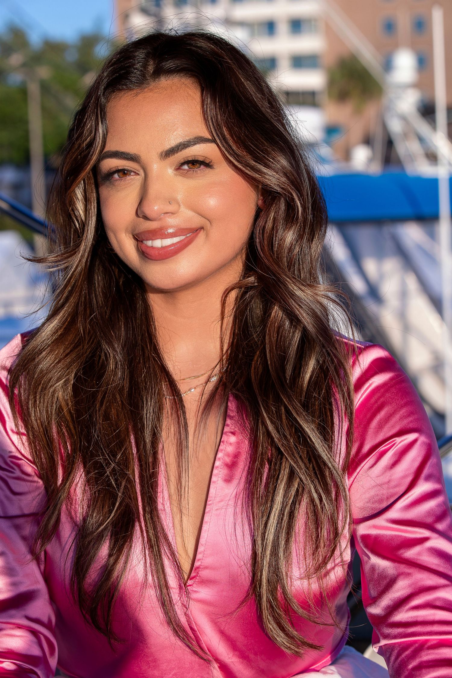 Portrait of someone wearing a pink satin top against a marina background.