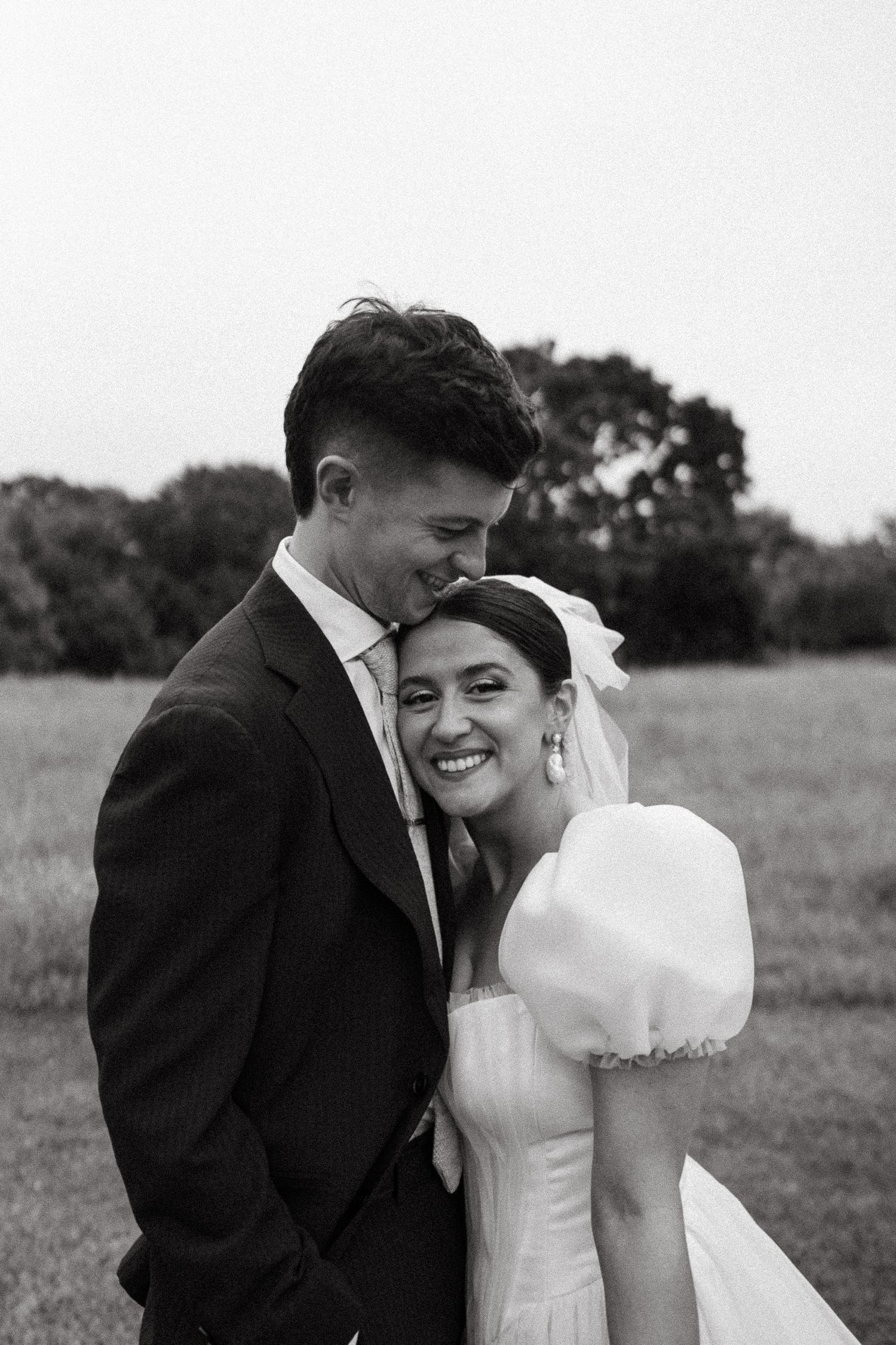 A couple in wedding attire walks down a rural path at sunset in black and white.