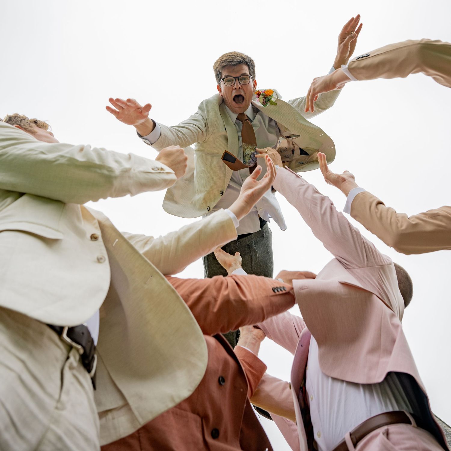 A group throws a person into the air during a playful wedding photo session.