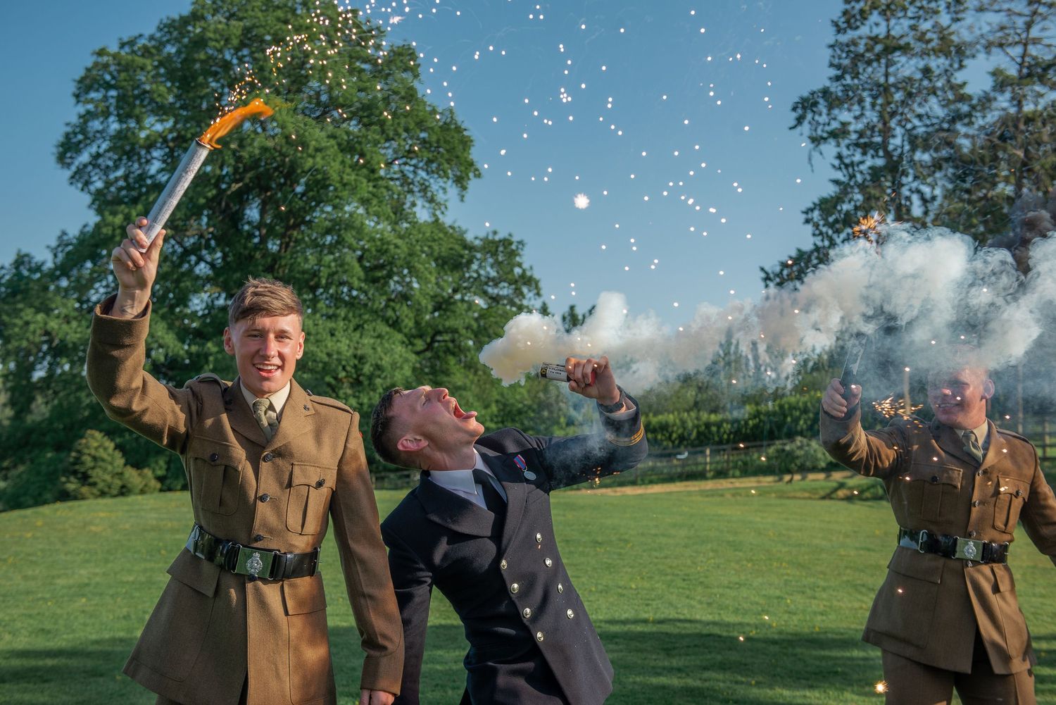 Military-uniformed performers creating celebratory effects with sparklers and smoke in outdoor garden setting.