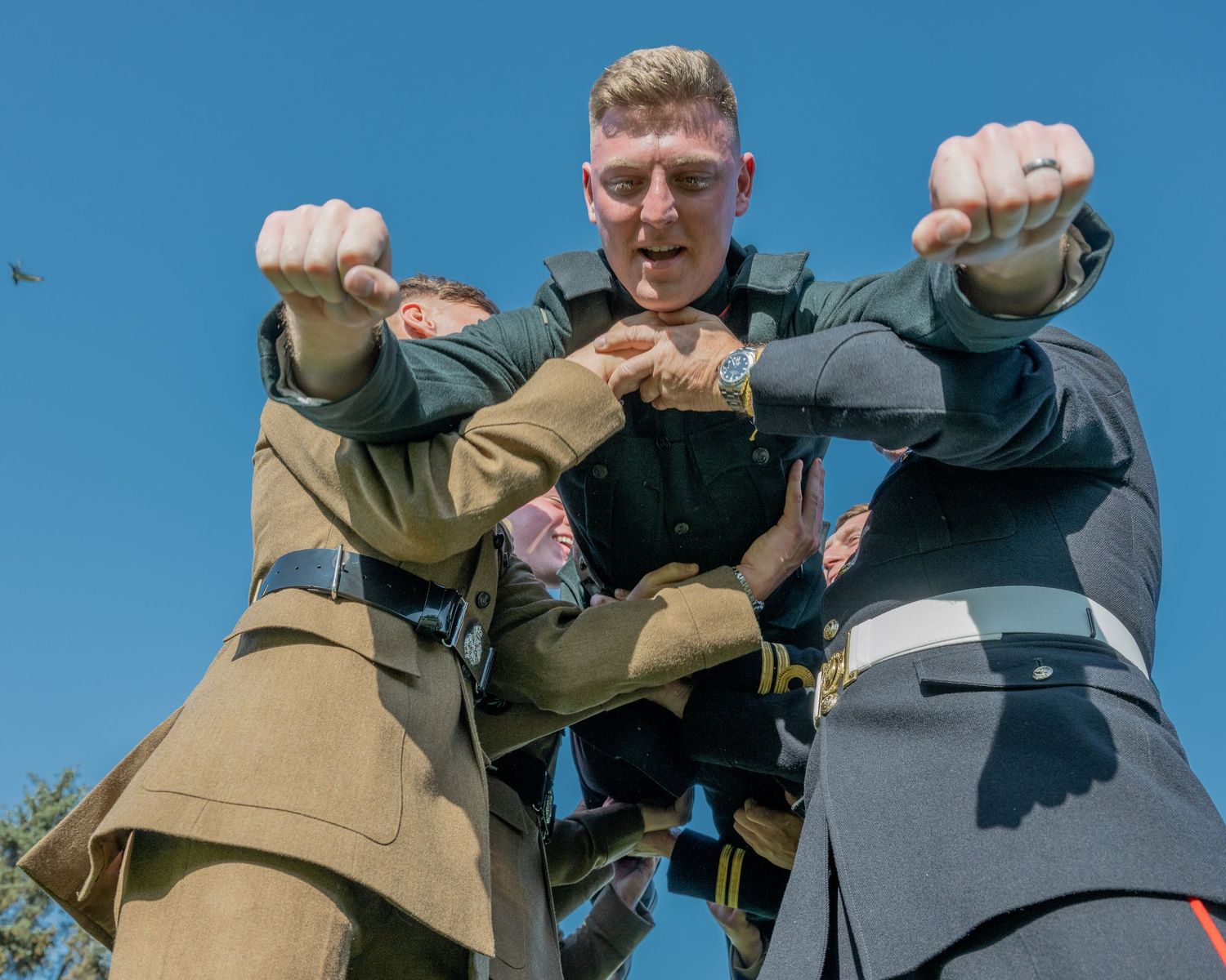 Three performers in vintage military uniforms posing dramatically against blue sky.