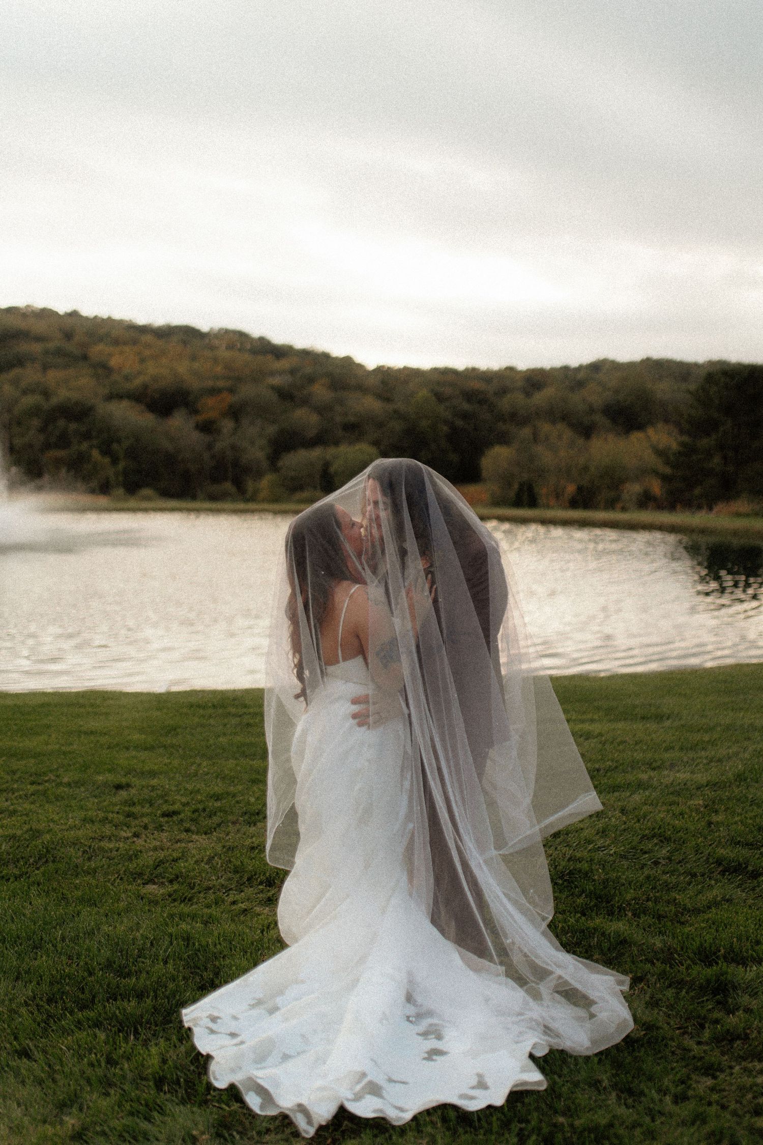 A wedding couple toasts with champagne glasses against a green hedge wall backdrop.