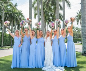 Bride and bridesmaids in light blue gowns celebrate outdoors holding colorful bouquets among tall palm trees.