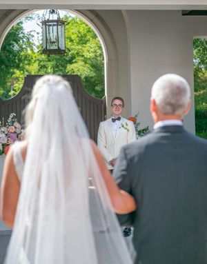 Bride walks down the aisle with her father toward the smiling groom waiting at a sunlit outdoor wedding ceremony.
