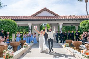 Joyful newlyweds celebrate after wedding ceremony at elegant outdoor venue with bridal party in blue dresses.