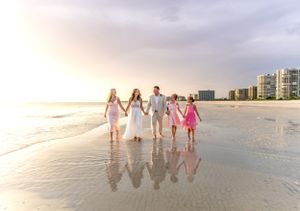 Wedding party walking together on beach at sunset with coastal buildings in background.