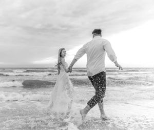 A couple splashing and playing together in the ocean waves at the beach in black and white.