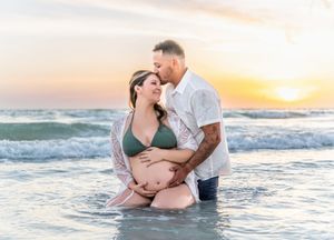 A romantic maternity photo shoot at sunset with a couple embracing in ocean waves.