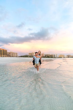 Two people enjoy a sunset beach photoshoot in the shallow waters of a tropical coastline with buildings in the distance.