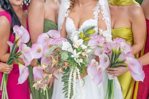 Bridesmaids in colorful dresses holding floral bouquets stand together at a wedding celebration.