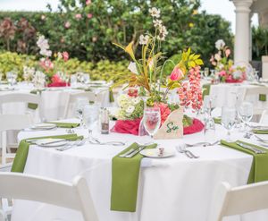 Elegant outdoor wedding reception tables set with white linens, green napkins and colorful floral centerpieces.