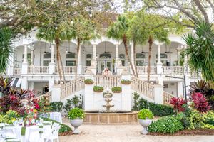A series of elegant white colonial-style buildings with verandas surrounded by lush tropical landscaping and palm trees.
