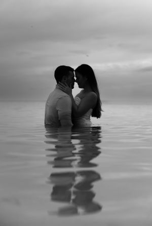 Intimate black and white portrait of couple standing in calm water at sunset.