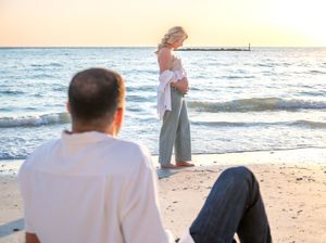 A couple enjoys a romantic moment at sunset on a beach with waves crashing in the background.
