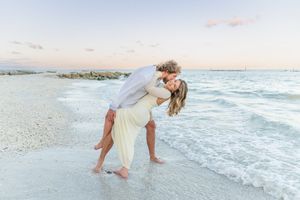 A romantic seaside moment with a couple embracing on a white sandy beach at sunset.