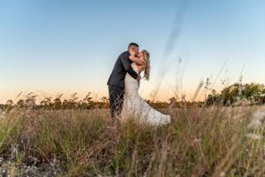 Romantic sunset portrait of newlyweds embracing in tall grass field.