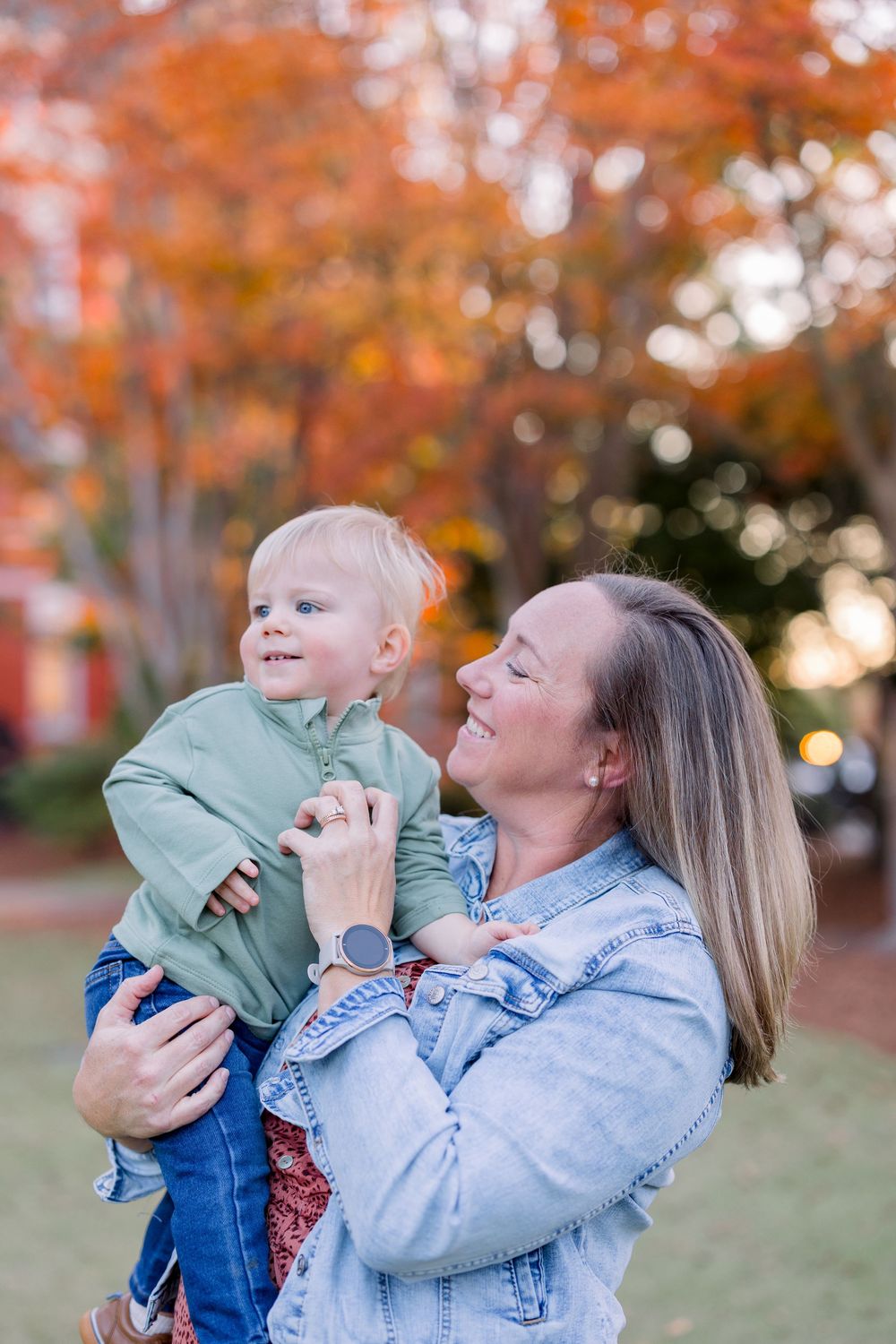A parent and child share joyful moments together outdoors during autumn with orange foliage in the background.