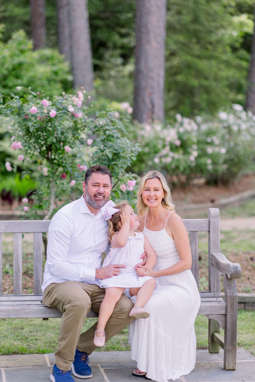 Family sitting together on a wooden bench in a garden setting with blooming flowers.