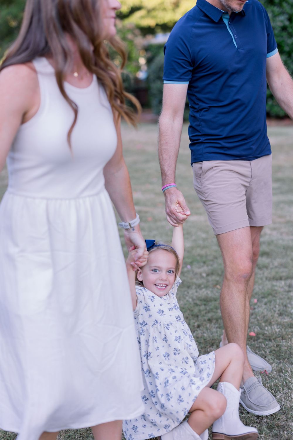 A family in coordinating blue and white outfits poses together outdoors on a grassy area during a photo session.