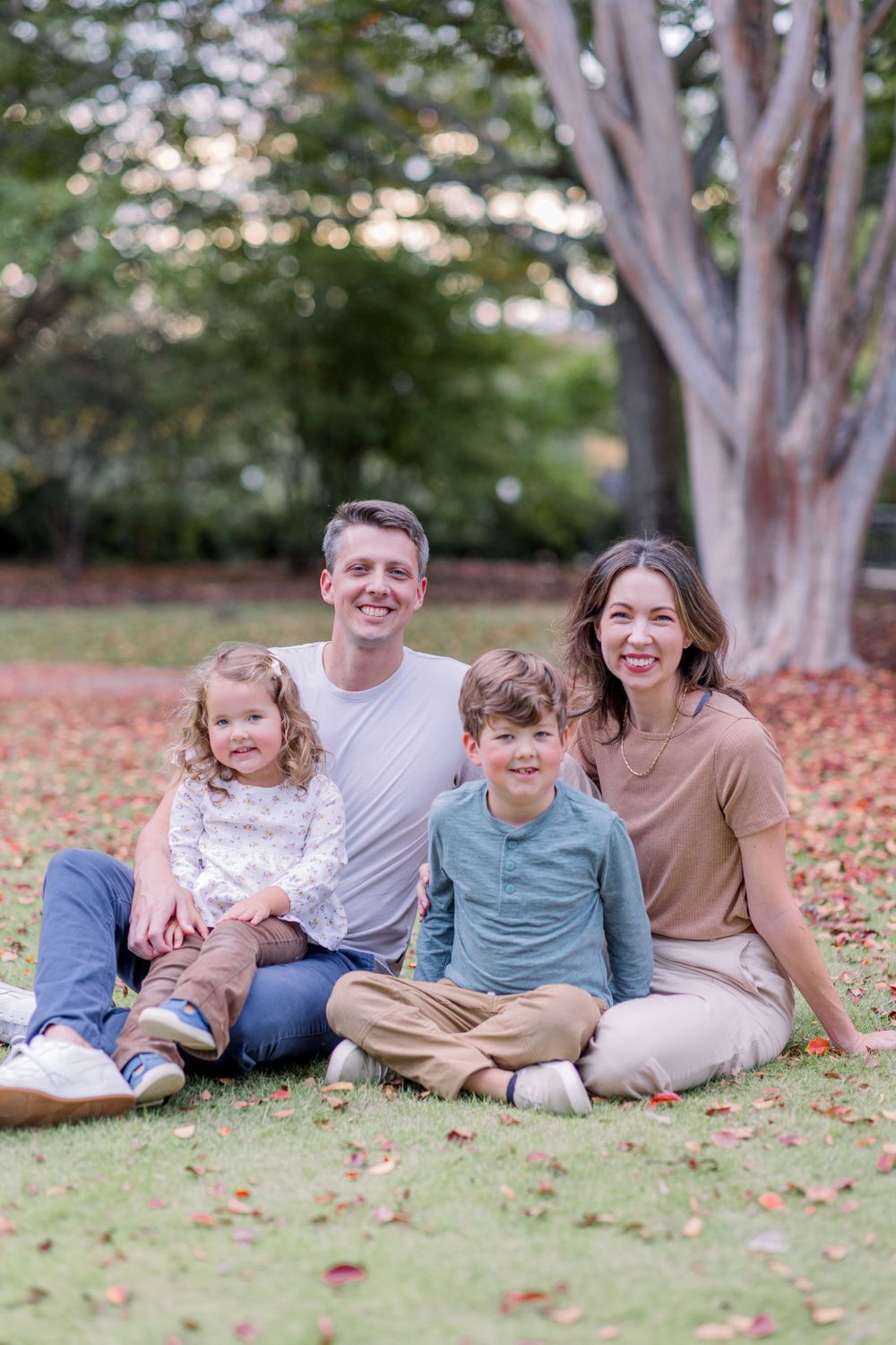 Family relaxes together on grass with beautiful trees in the background.