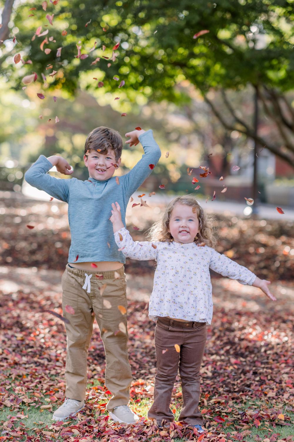 Children play and throw leaves in a scenic autumn setting with fallen foliage.