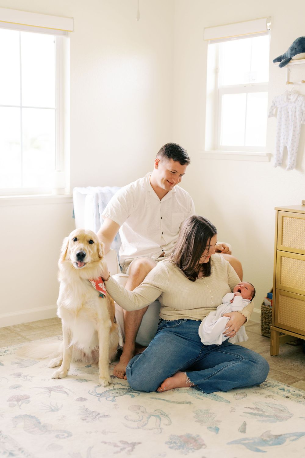 Family with newborn baby and golden retriever dog sitting together in bright nursery room.
