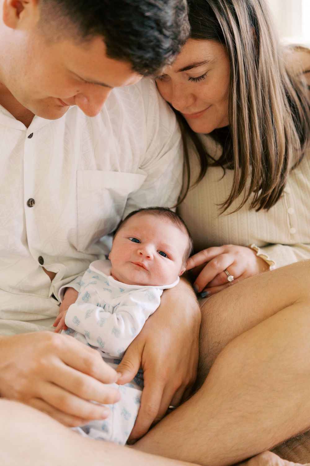 New parents lovingly gaze at their newborn baby, cradling the infant in a warm, intimate family portrait.