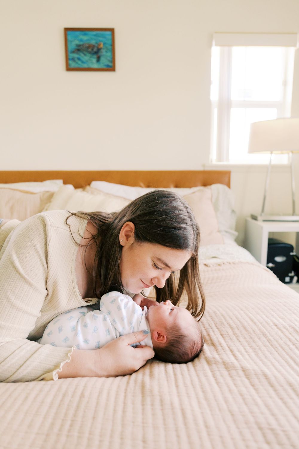 A mother tenderly gazes at her newborn baby lying on a bed, sharing a sweet moment in a cozy bedroom.