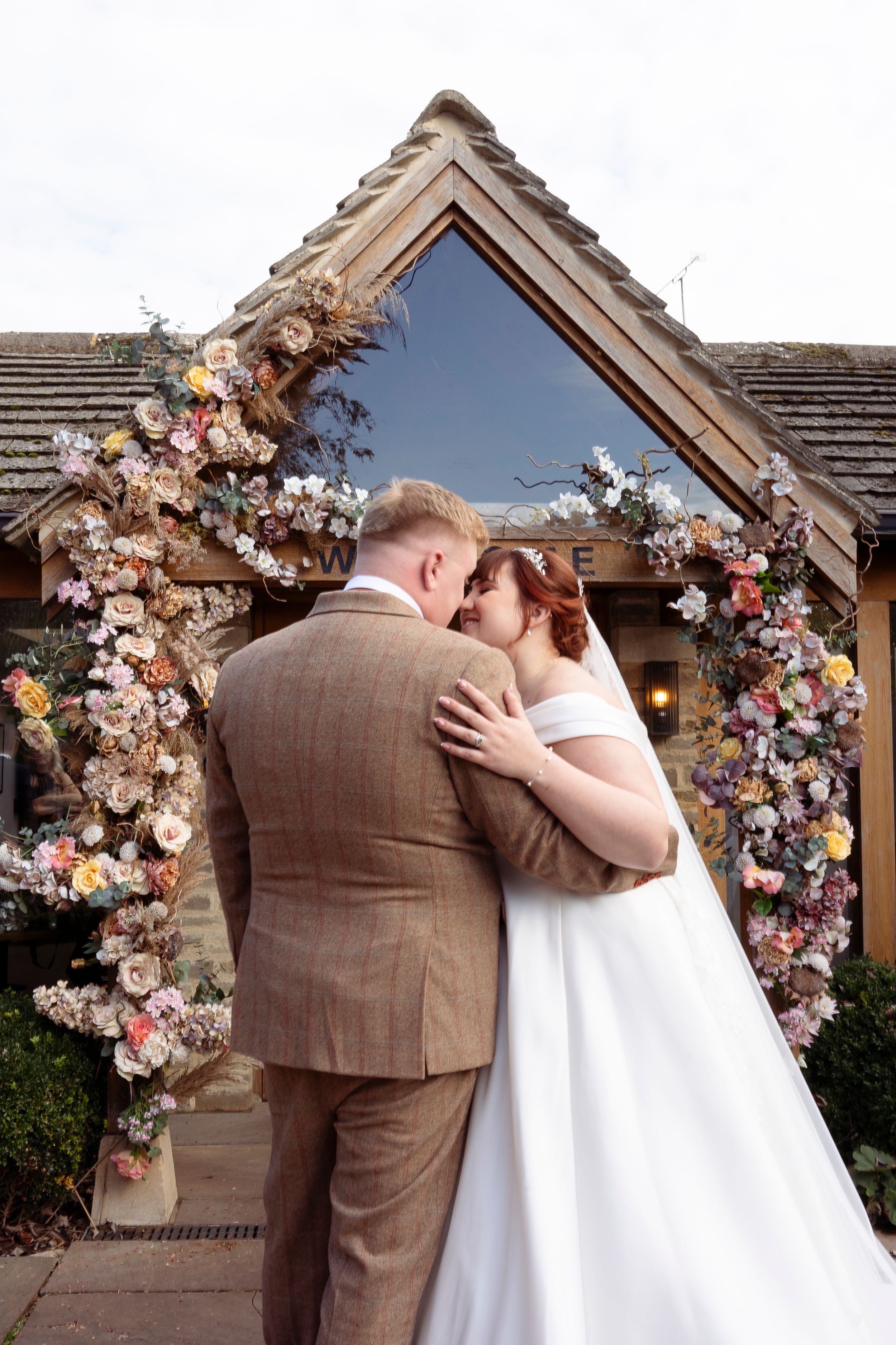 Romantic wedding kiss under floral arch with dried flowers and fresh blooms.