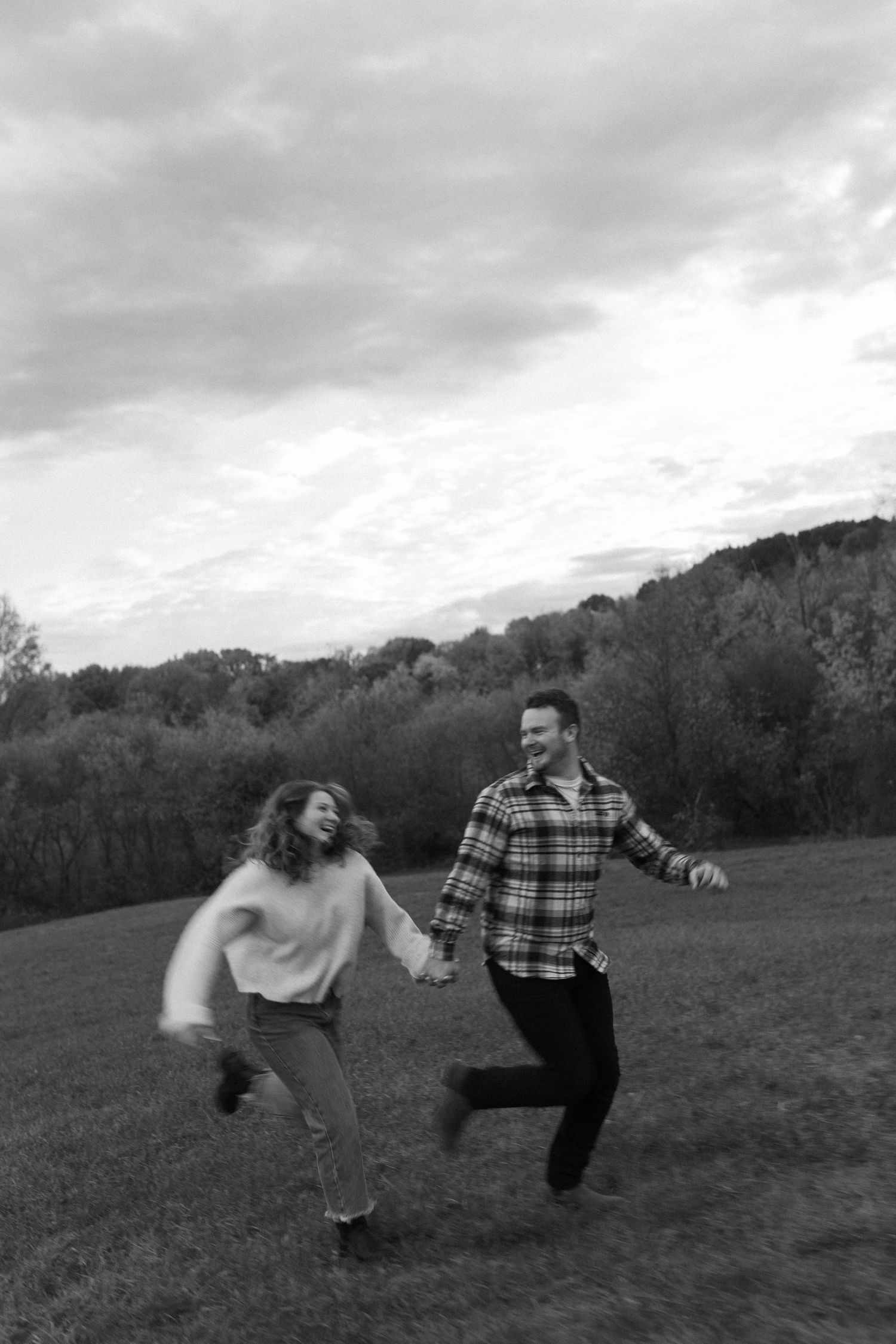 Black and white photo of a playful couple running and laughing together in an open field.