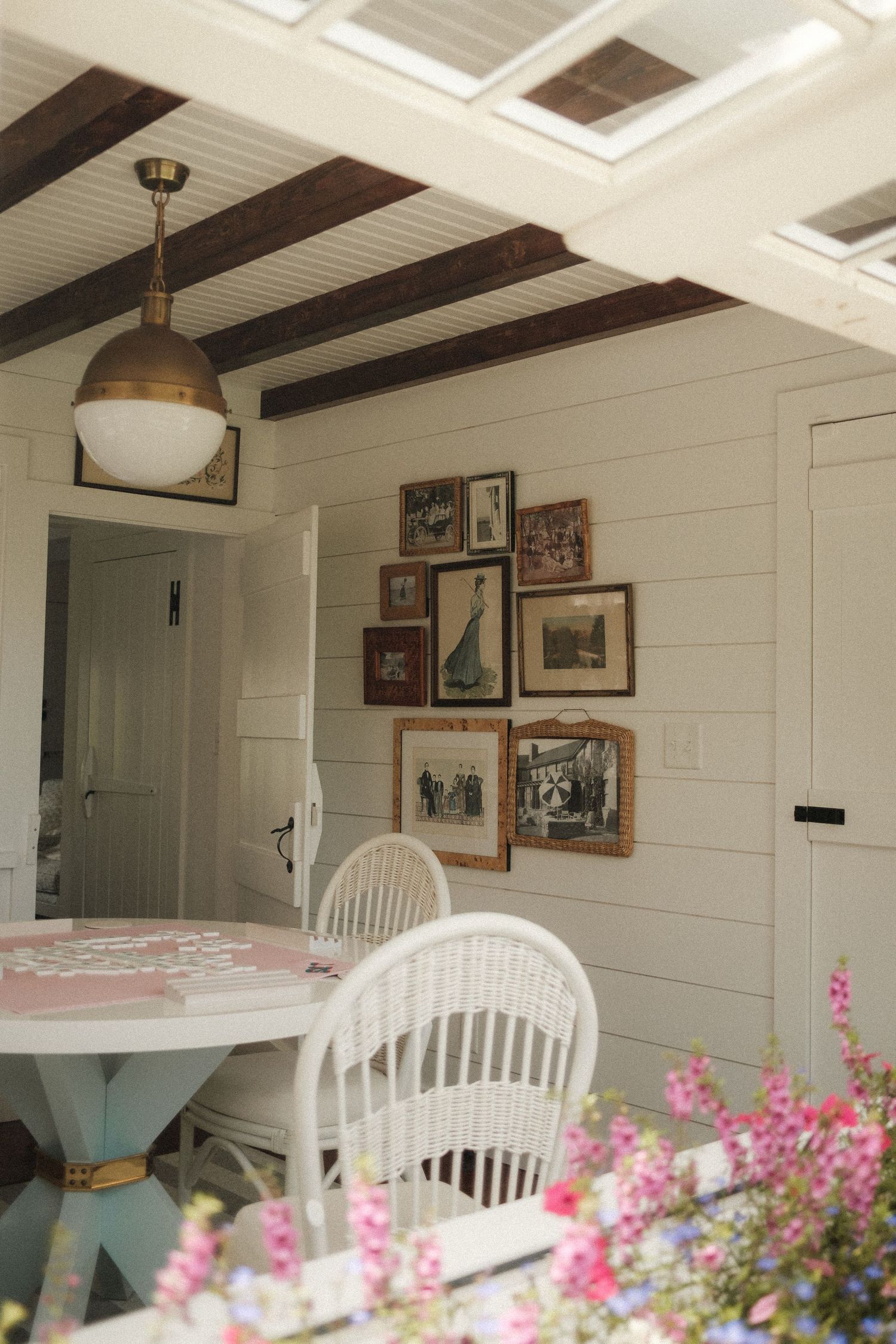 White farmhouse interior with exposed beams, vintage photos, and windsor chairs under skylights.