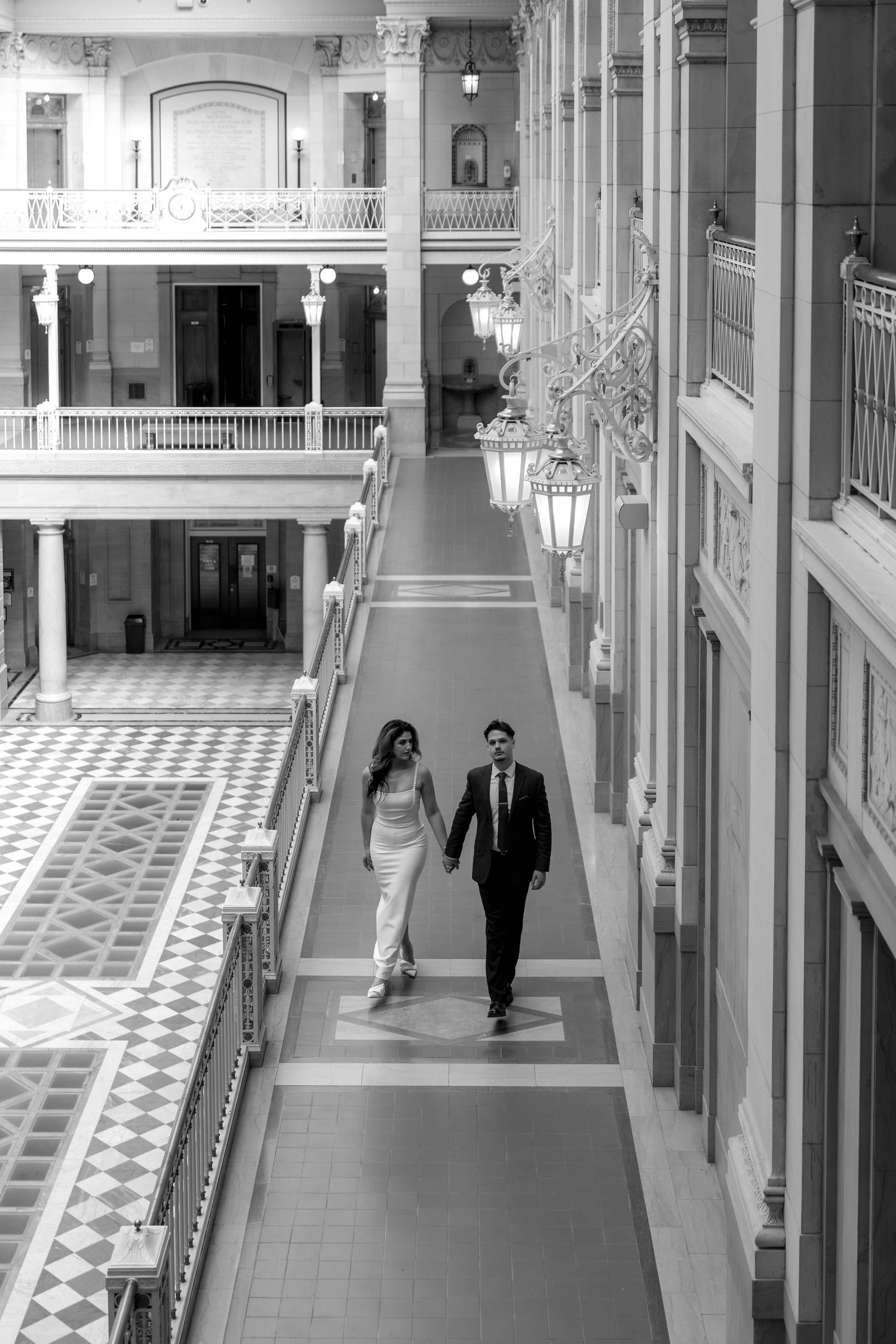 Black and white hallway with checkered floor pattern showing figures walking through an elegant corridor.