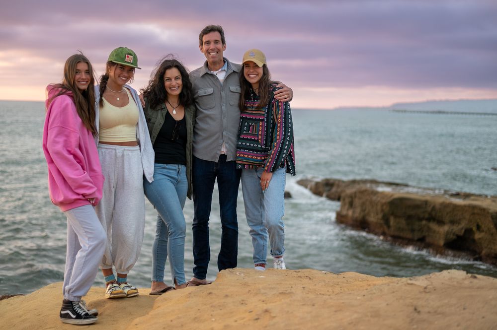 Group of friends posing together on rocky coastal cliff during sunset.