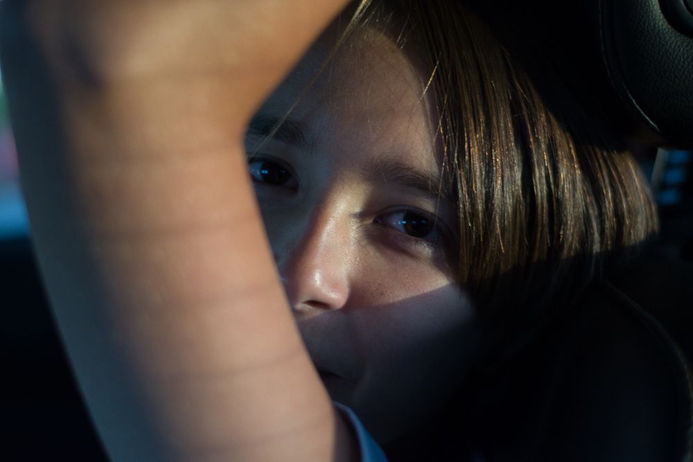 Close-up shot of a person looking through a car window in dim lighting.
